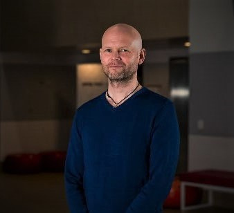 A portrait photograph of Andi Nygaard, a man in a navy blue pullover