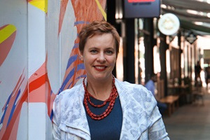 A portrait of Cara Wood, a woman smiling in front of a colourful mural.