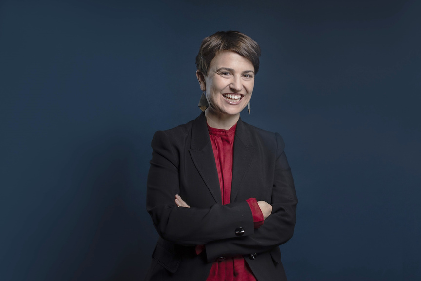 A portrait photograph of Vanessa Pillar. A woman wearing a red shirt and black blazer, smiling with arms crossed.